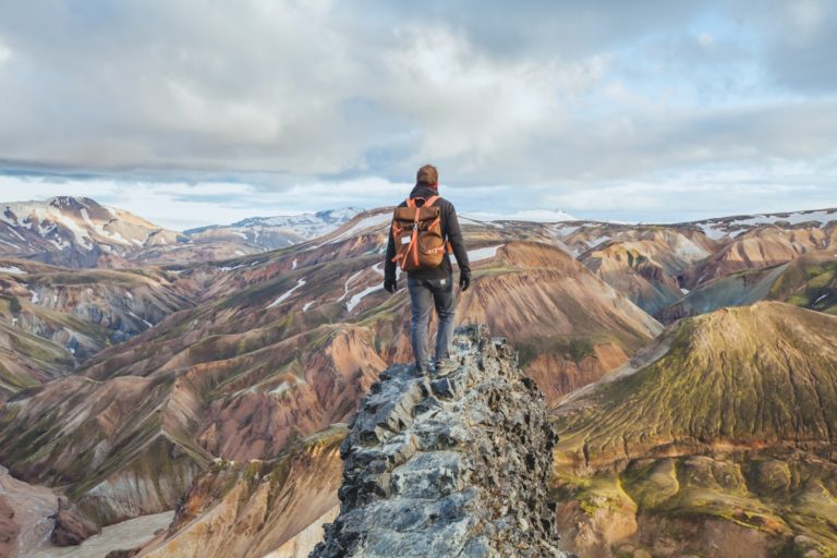 adventure travel, hiking in Iceland with backpack, tourist looking at colorful landscape of Landmannalaugar