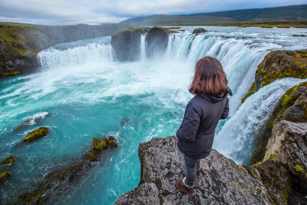 A young tourist looking at the Godafoss waterfall from above. Iceland