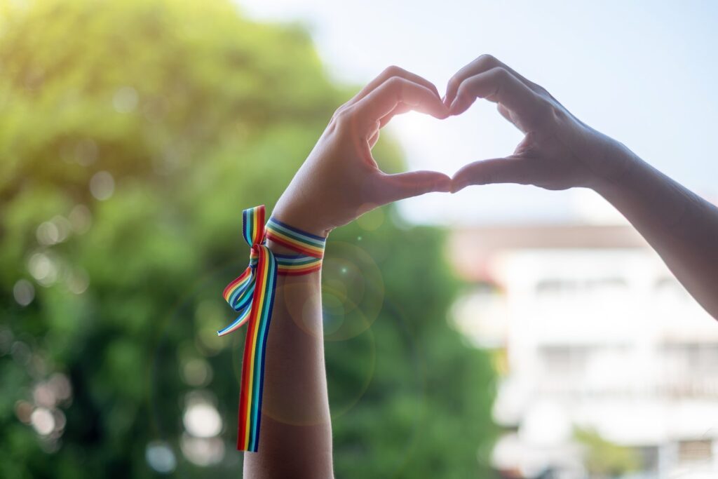 woman hands showing heart shape sign with LGBTQ Rainbow ribbon in the morning for Lesbian, Gay, Bisexual, Transgender and Queer community