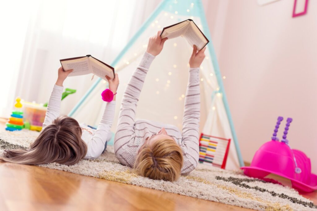Mother and daughter lying on a playroom floor, reading books. Focus on the mother