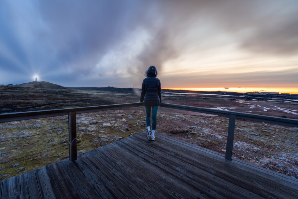 Woman posing at a lighthouse and smoky lands in Iceland. Midnight Sun concept.